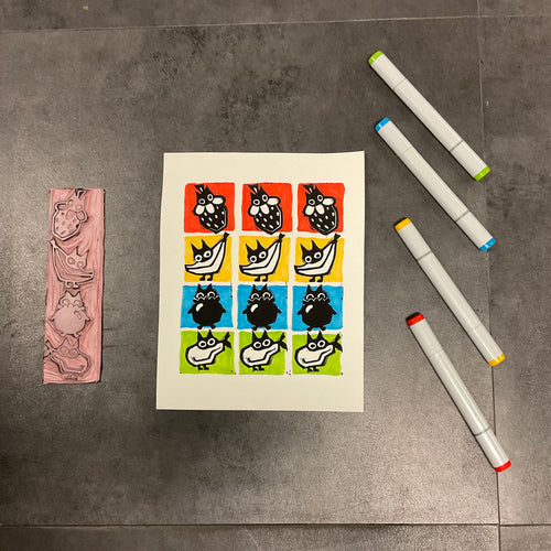 Sheet of printed cats as fruit on the floor with markers and a stamp.