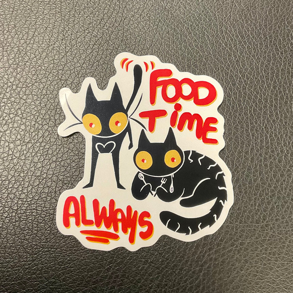 Sticker of two cats with the words FOOD TIME ALWAYS around them on a flat surface.